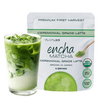 A pouch of Encha Matcha Ceremonial Grade Latte next to a glass of iced matcha latte with milk on a white background.  _30g (1.02oz) 15 cups